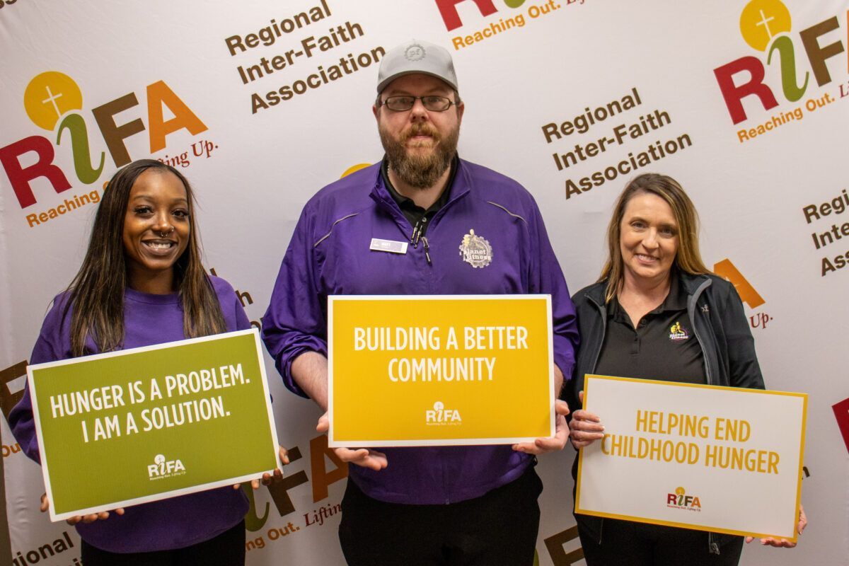 Three people holding signs related to combating hunger.