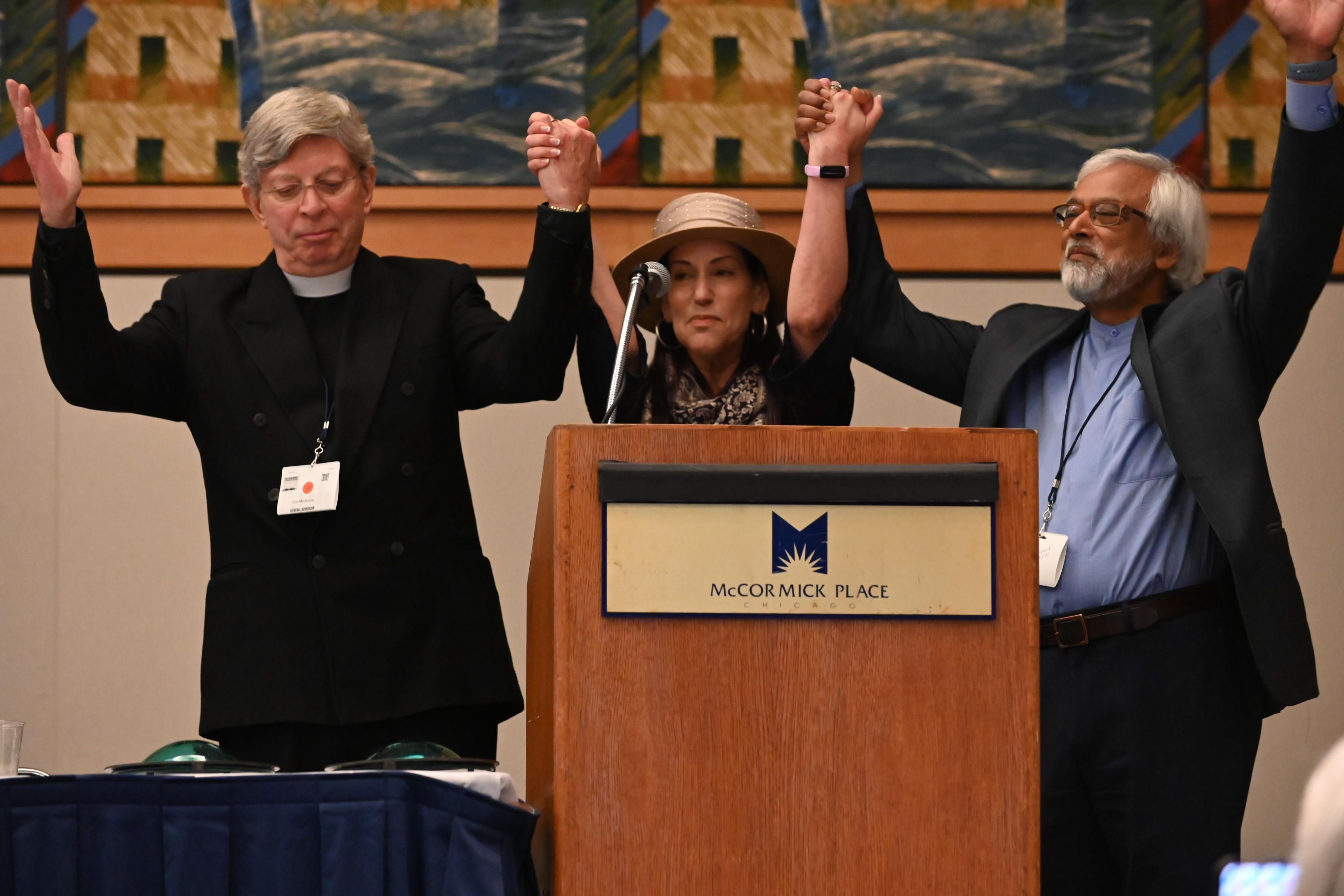 The Three Interfaith Amigos holding hands, with arms raised, after giving the invocation at the Compassion Banquet 2023.