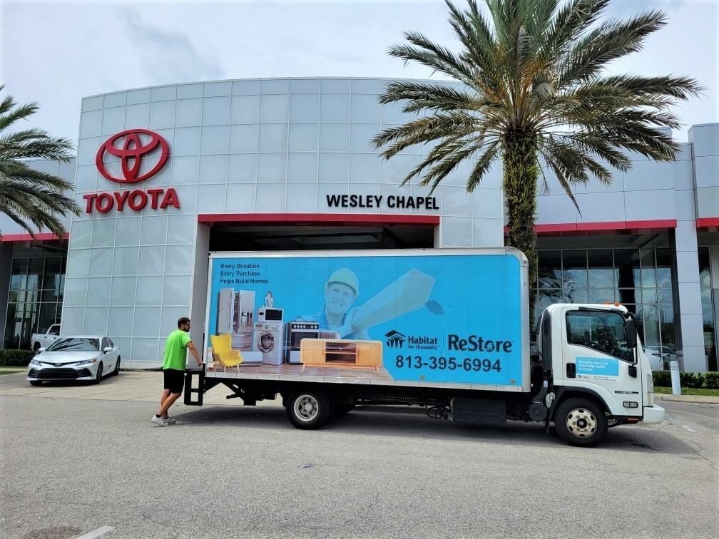 Habitat for Humanity ReStore donation truck parked at Toyota Wesley Chapel with staff member unloading items for community donation pickup.