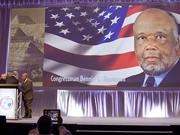 Stage with a large screen displaying a man’s portrait, an American flag, historical imagery, and the text "Congressman Bennie G. Thompson."