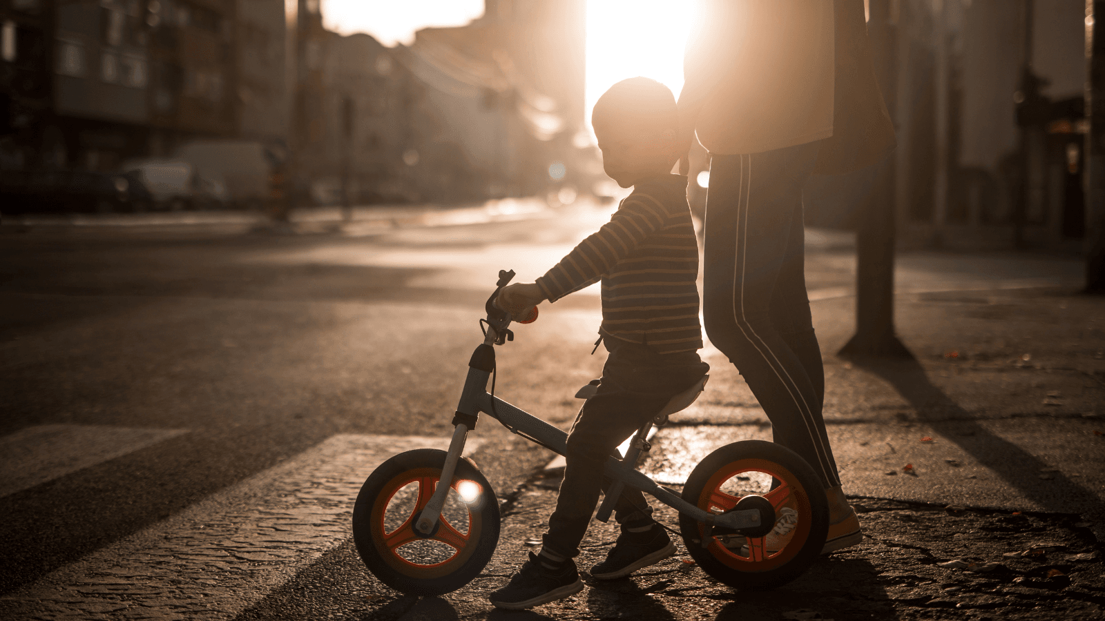 Child on bike and parent walking on city street