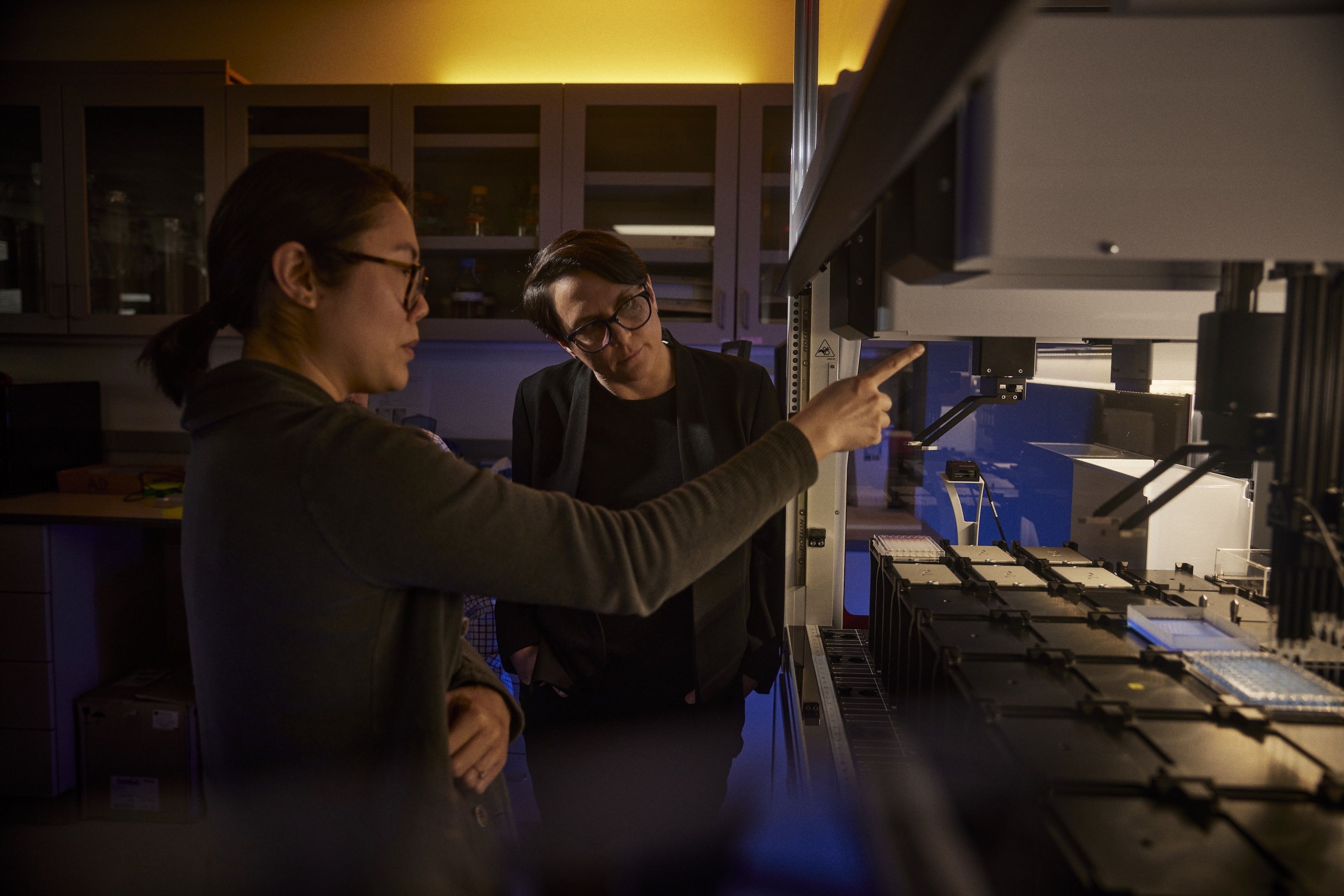 Two scientists at work in a lab where a robot streamlines genetic sample processing