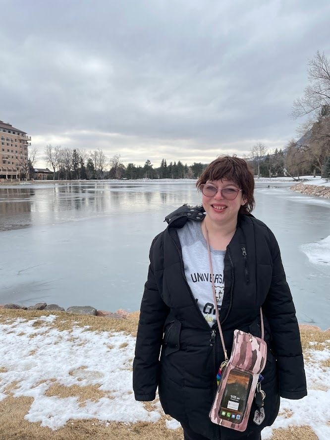 Katelyn wears a jacket in front of an icy pond. There is snow of the ground.