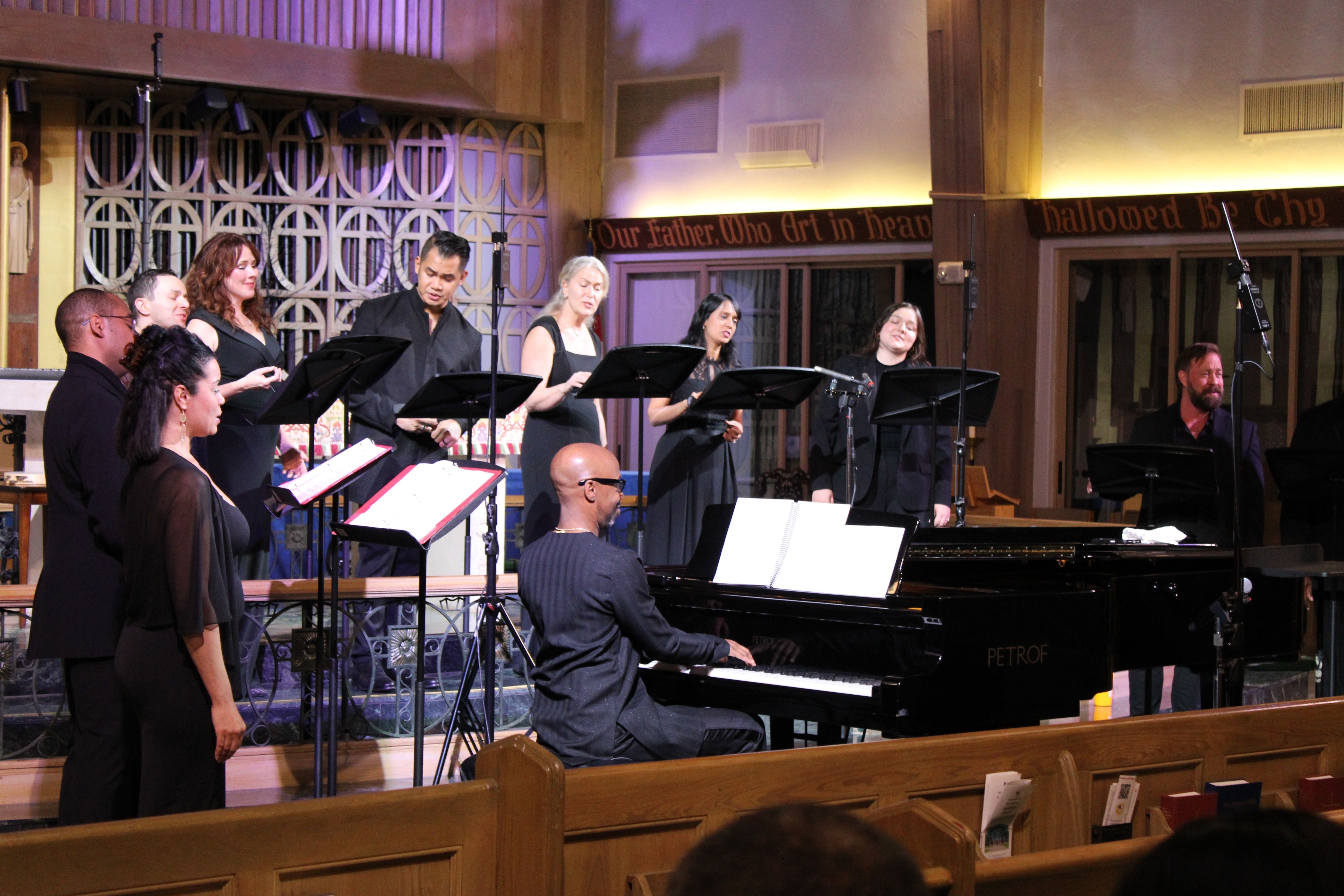 Seraphic Fire singers surround conductor Jason Max Ferdinand playing the piano on a church alter.