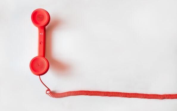 Photo of a retro corded telephone handset, bright red on a white background. The handset is on the left side of the photo with a red cord extending out to the right across the photo.
