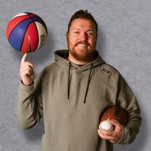 Mark smiling at the camera holding a basketball, football and baseball