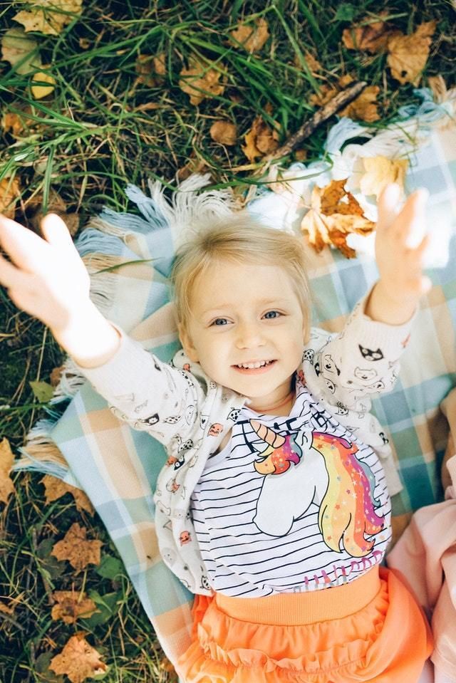 Child laying down on blanket with fall leaves