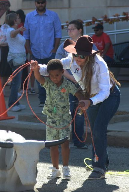 Woman volunteer in cowboy clothes teaching a young boy how to rope a steer model.