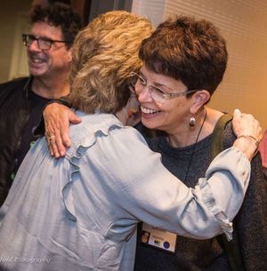 Two women hugging. The one facing the camera is smiling.