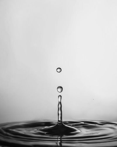 Black and white photo of water droplet creating ripples across the surface of a pond or puddle.