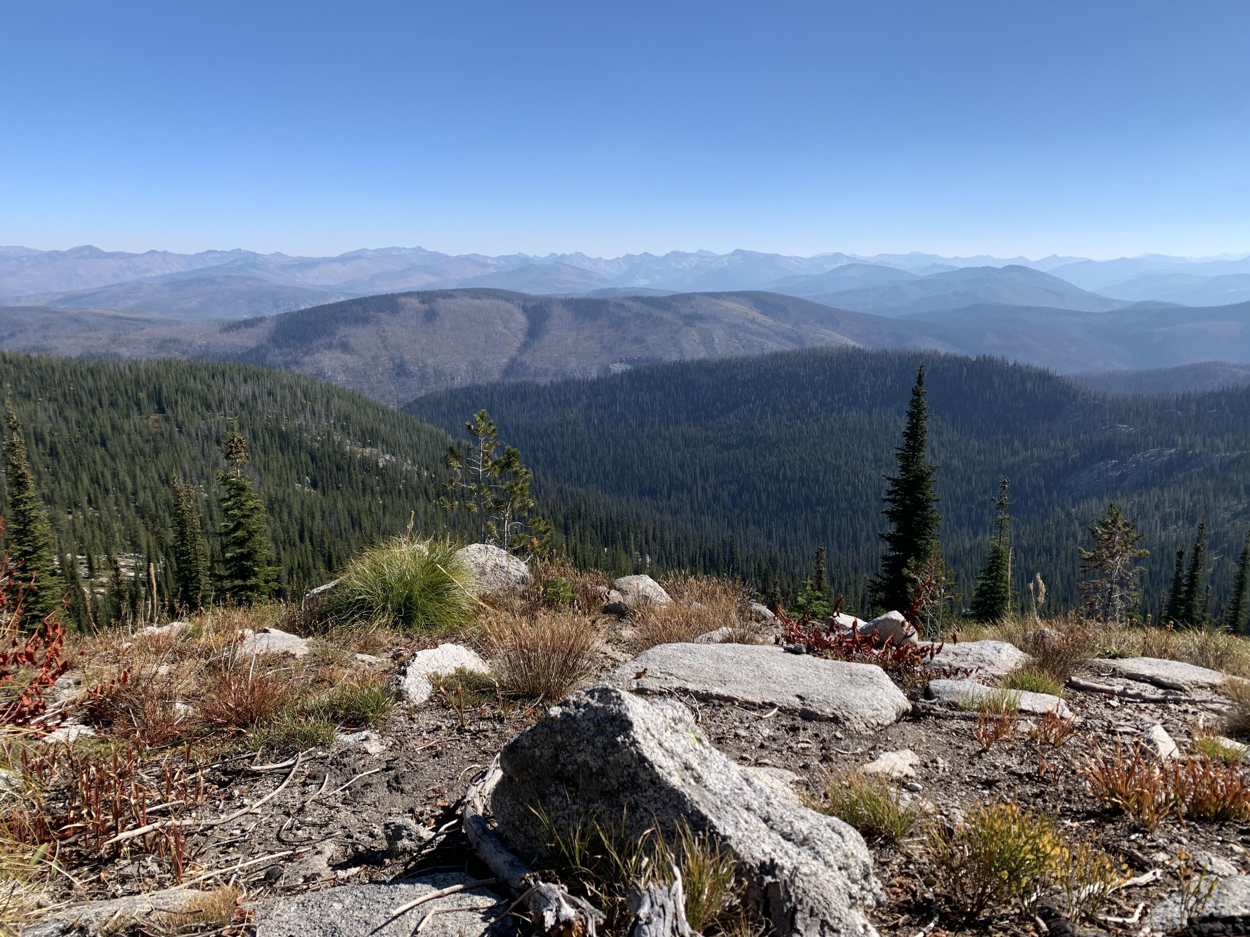 A view overlooking a valley, with mountains and blue sky in the distance.