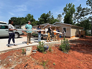 Volunteers carrying lumber across a dirt yard at a build site