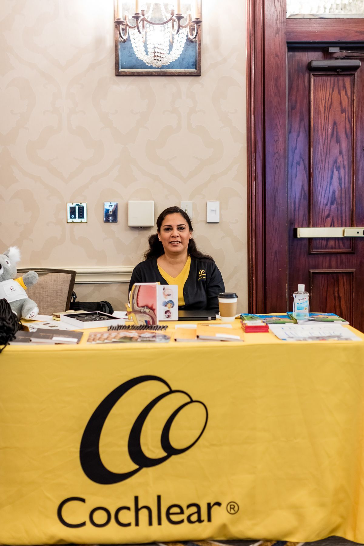 A representative from Cochlear sitting at a table with the yellow Cochlear banner. 