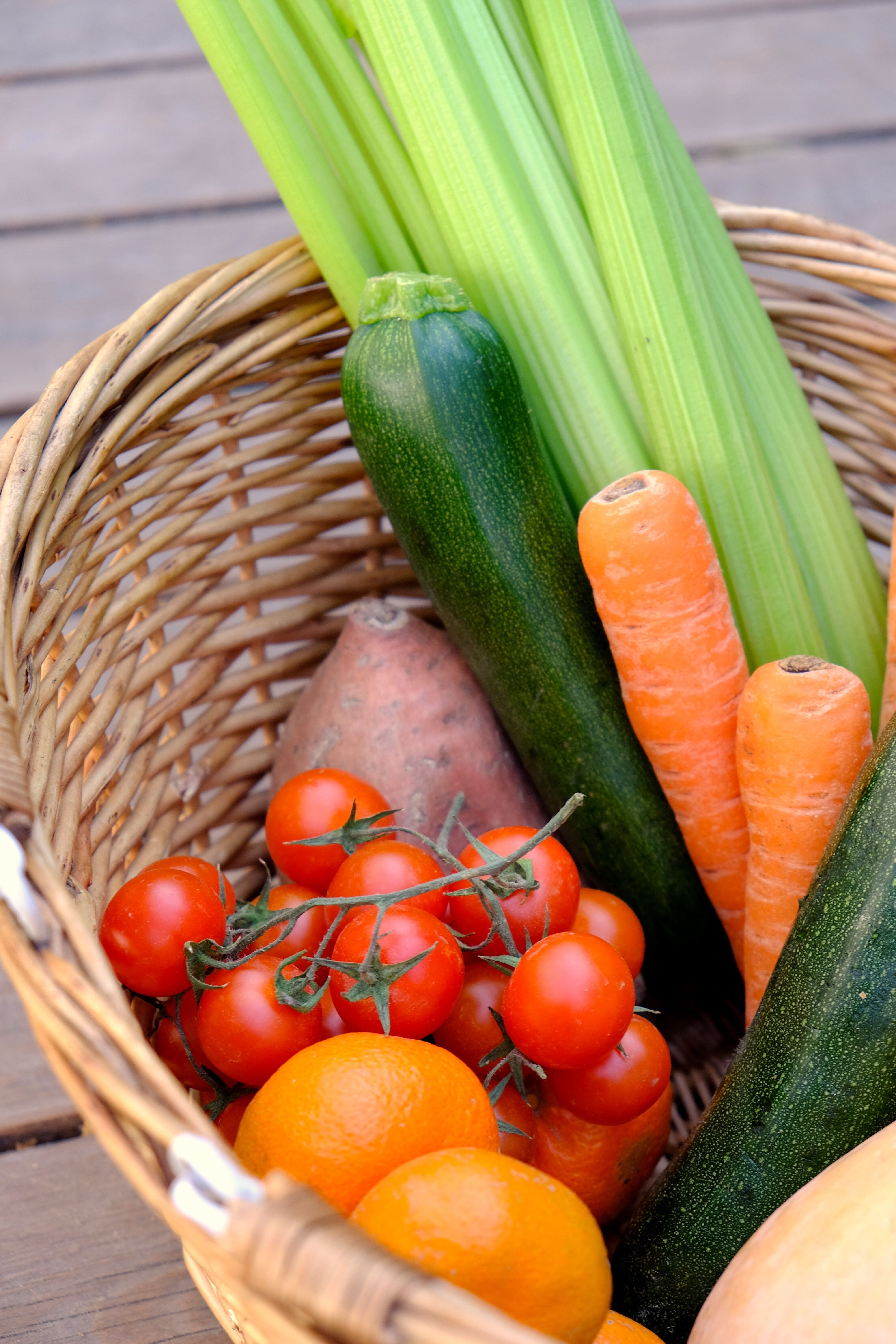 A wicker basket holds tomatoes, carrots, celery, zucchini, and a sweet potato.
