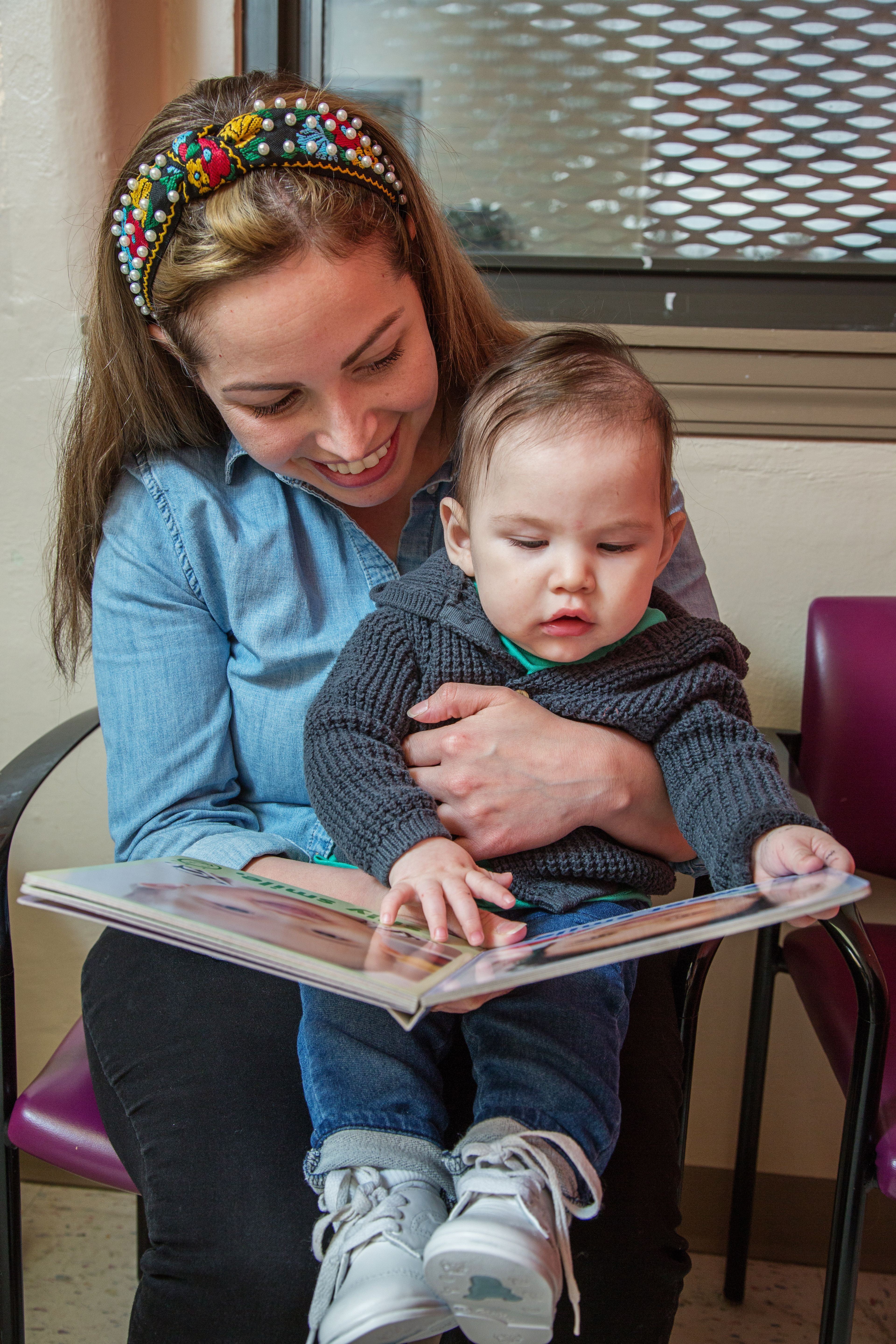 Mother and infant sit in chair and look at book together