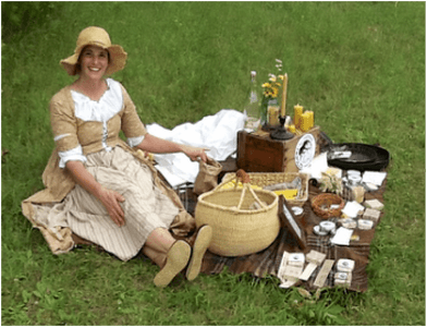 Woman dressed up in pilgrim clothes sitting with a picnic outside.
