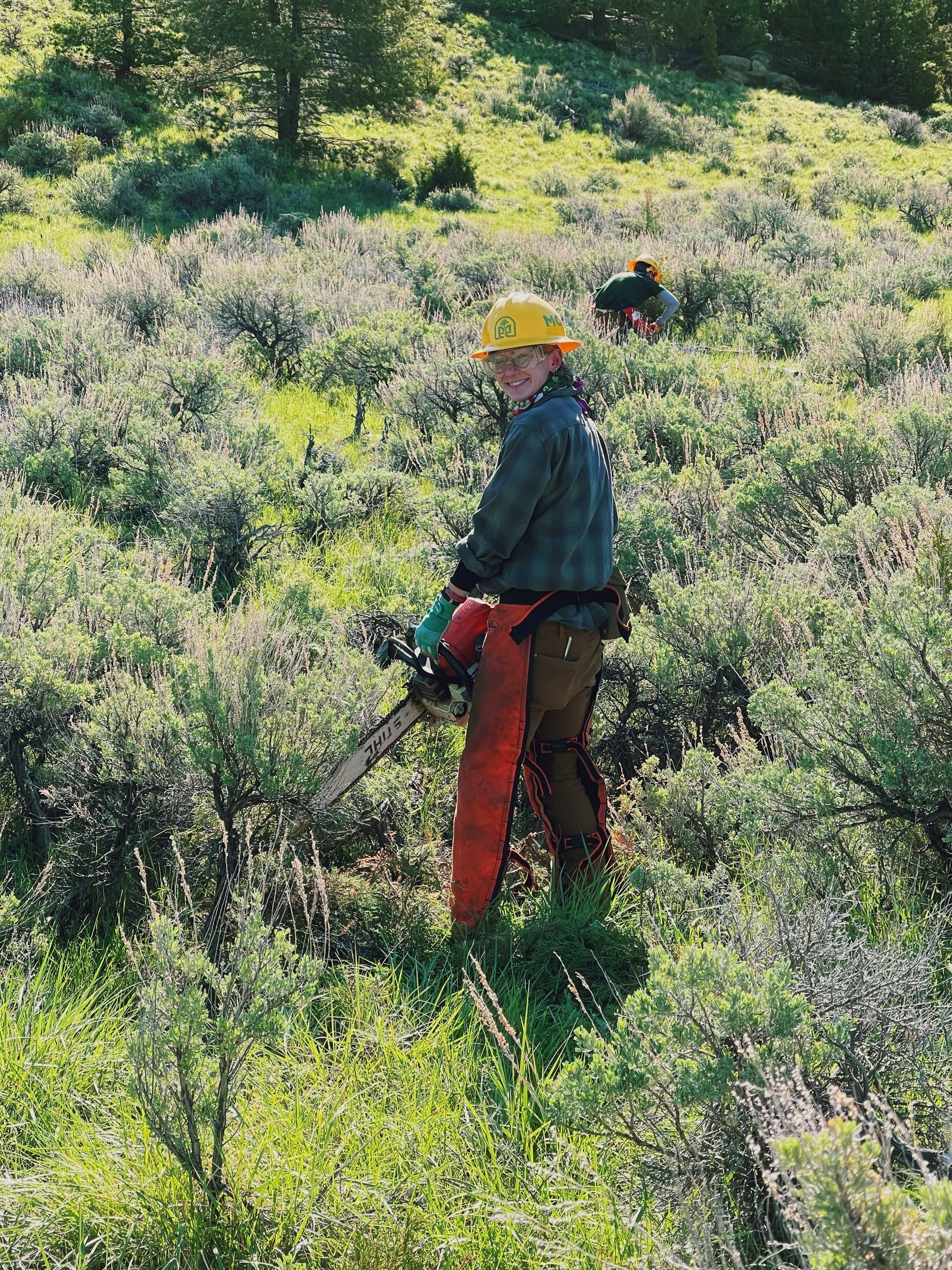 A women's crew member stands in a sage brush field