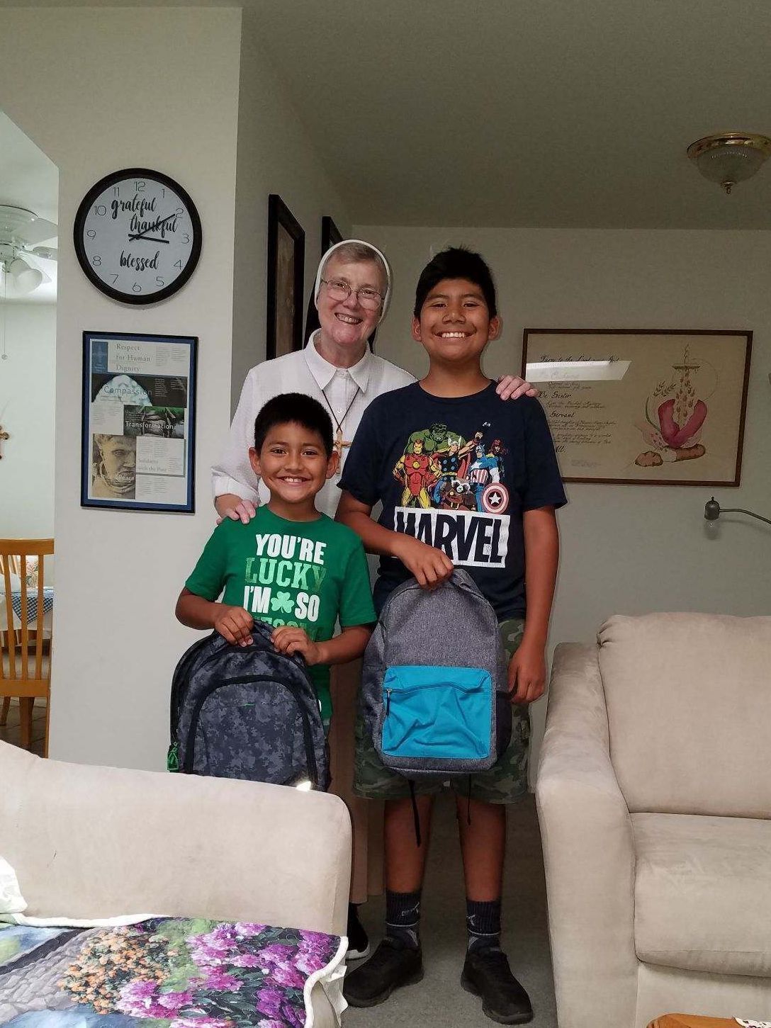 Sister stands behind two school aged children holding backpacks