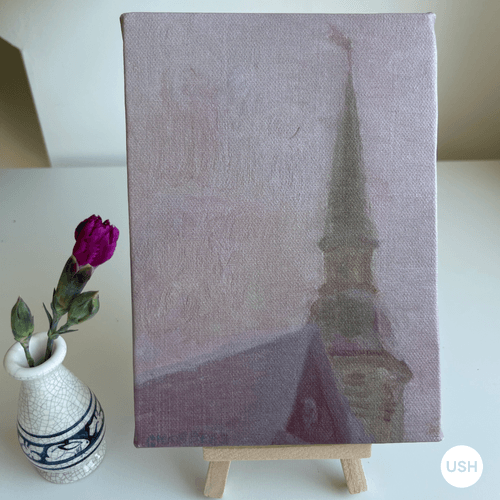 Painting on canvas, with a pink background and tower in the foreground. Next to the canvas is a rose in a vase.