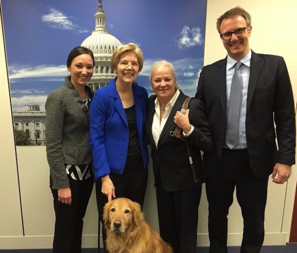 A photo of Krista Vasi, Mark Dunning, and Moira Shea with her guide dog Finnegan with Senator Elizabeth Warren