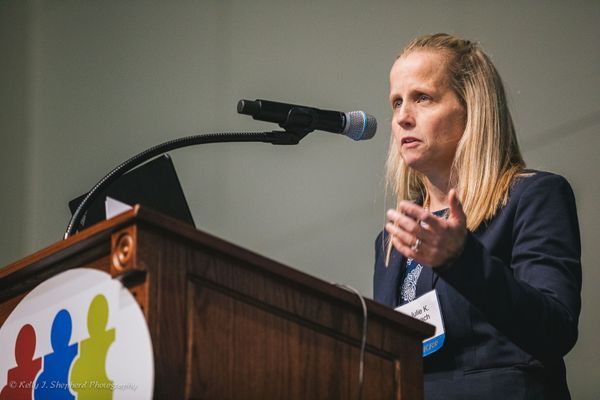 A female medical providers stands at a microphone behind a podium with a PSC Partners logo on the front.