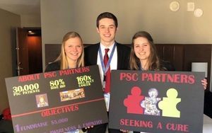 Three young adults (girl, boy, girl) stand in a line. They are holding fundraising signs for PSC Partners.