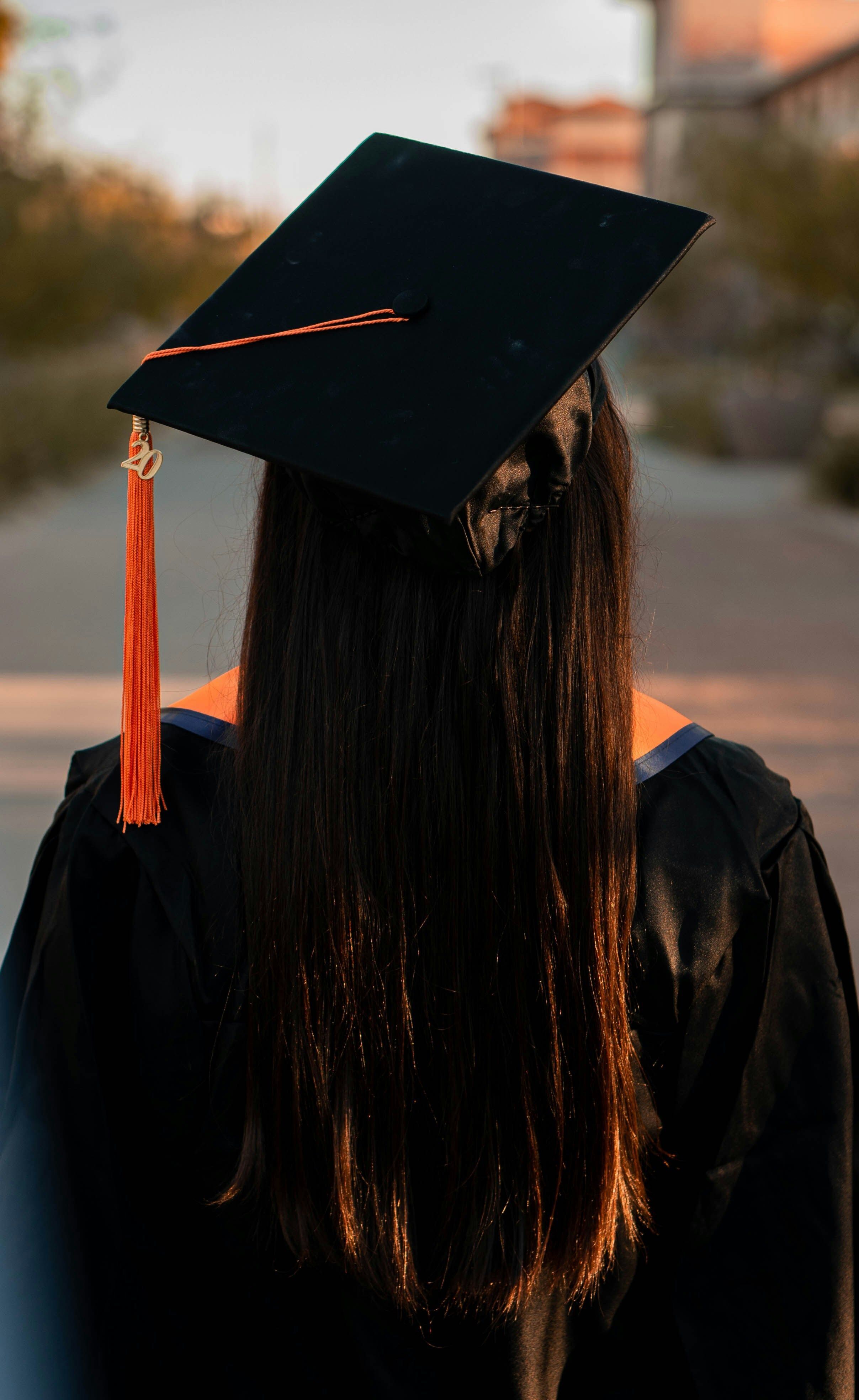 person with long black hair wearing a black graduation cap and gown