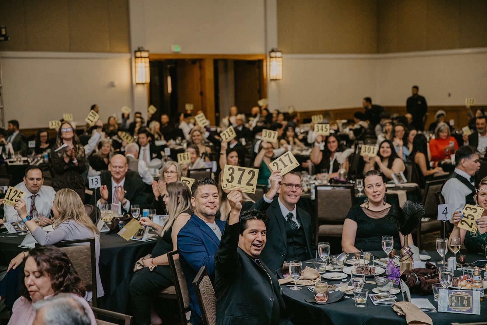 A packed ballroom of guests at the Mapleton Education Foundation Gala raising their bidder paddles in excitement, celebrating and supporting student dreams.