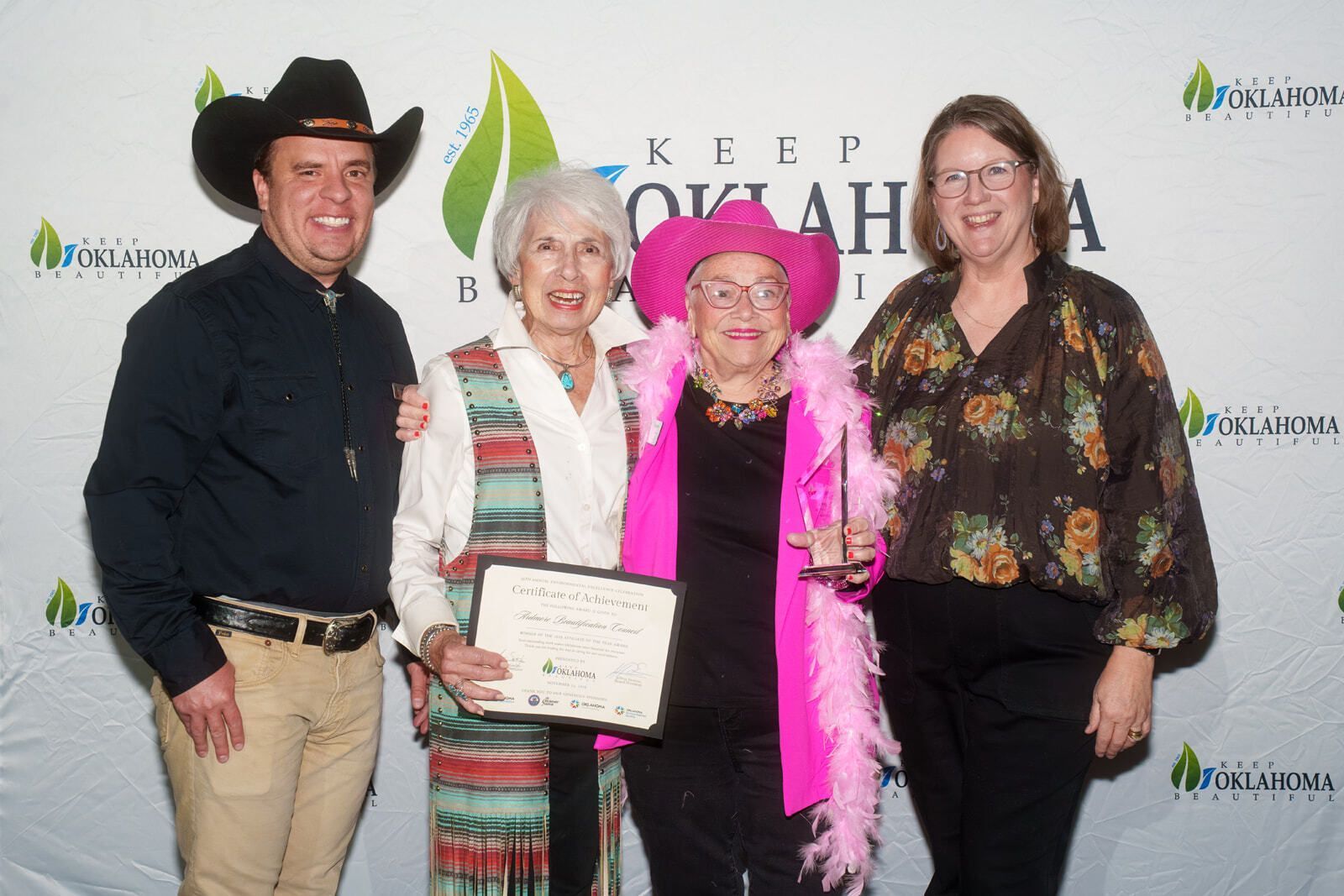Four smiling people in western-style formal wear. Two of them are holding awards