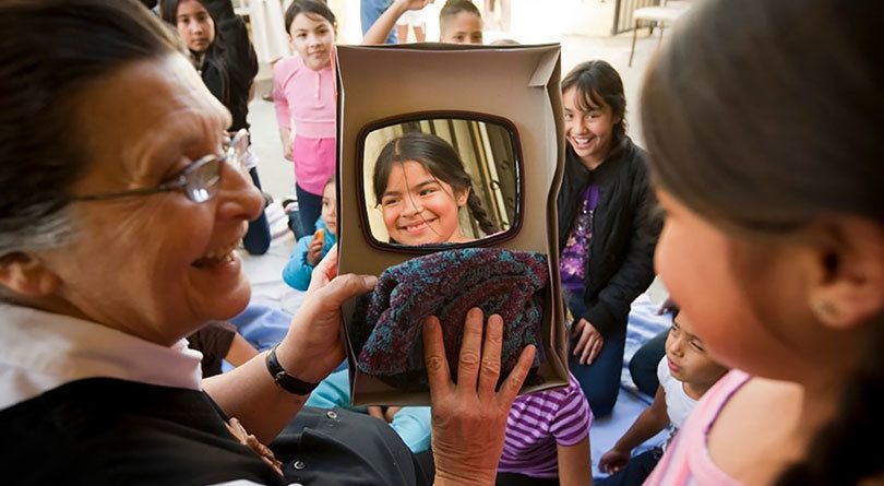 Sister Carol Marie holds a mirror for a young girl in Pomona