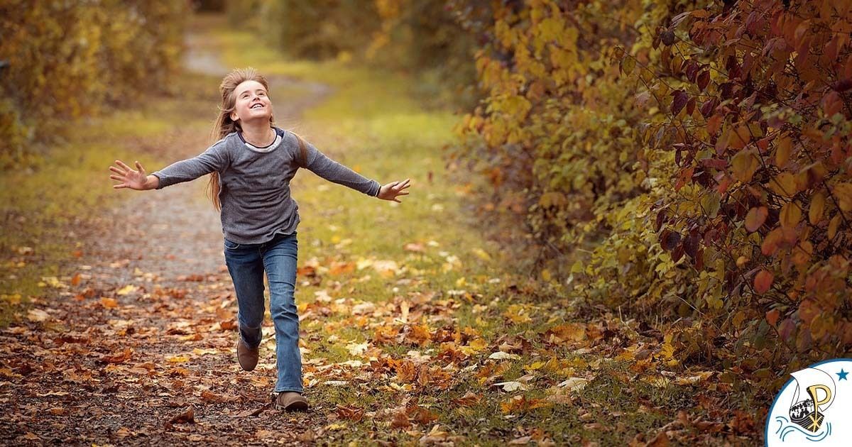 As she walks through fallen leaves a young girl smiles with relief and her arms extended as she looks toward the sky