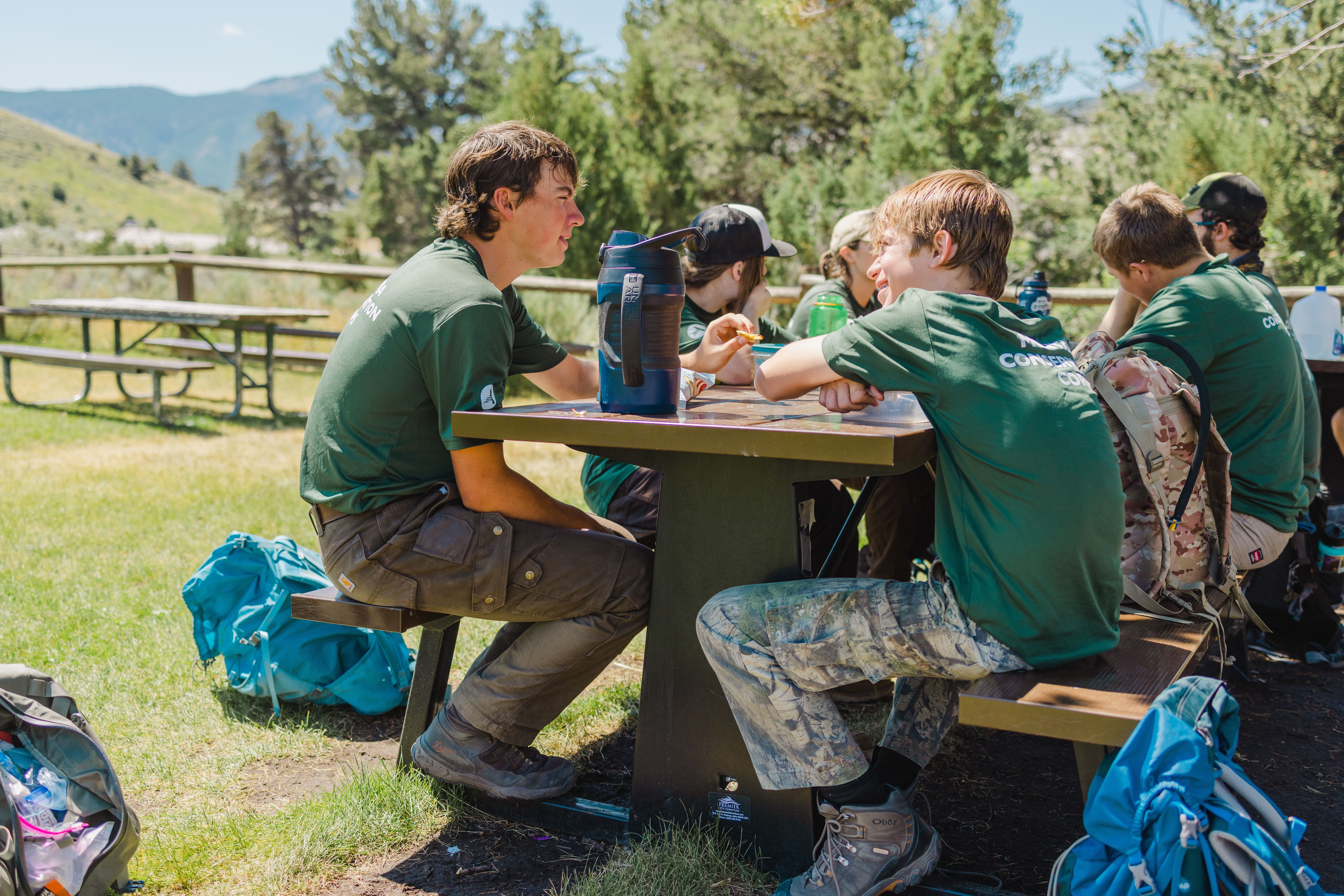[Image description: Two MCC members are walking away from the photographer, leading into a trail along a river, cut with large towering rock features.]