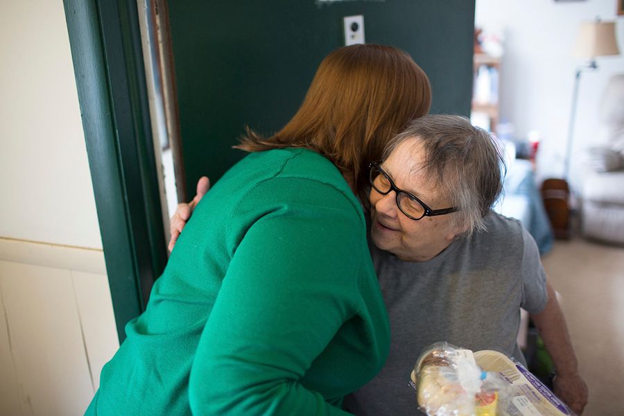 Older woman smiling and hugging volunteer who delivered her meal