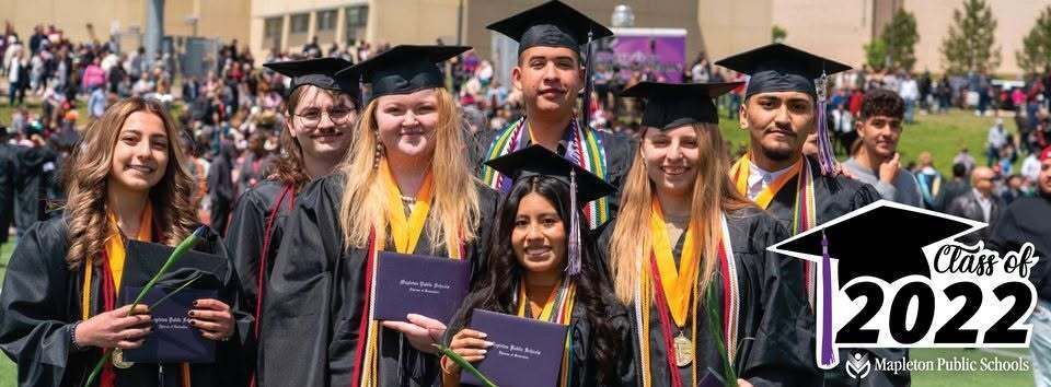 Graduating students wearing caps and gowns smile while holding their diplomas.