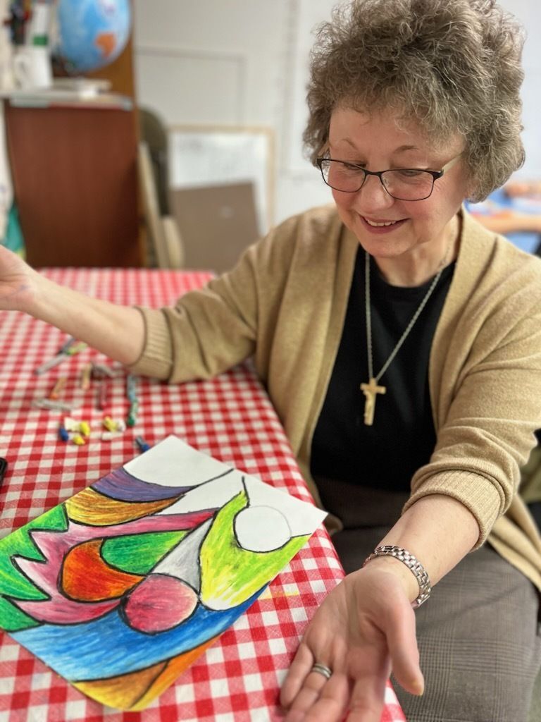 Sister Jeanine sits at a table with a craft project in front of her.