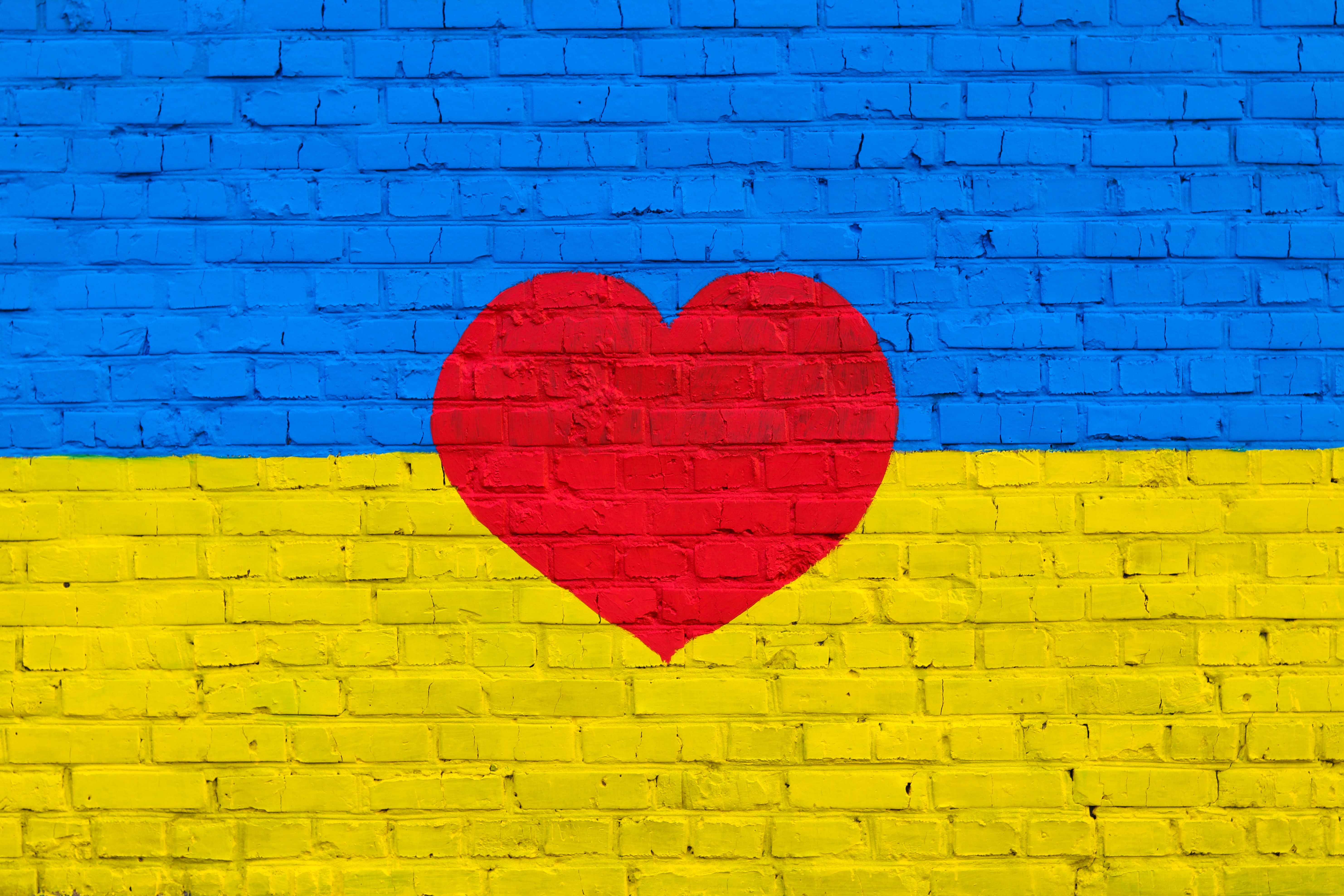 Brick wall is painted yellow and blue in the colors of the Ukrainian national flag, with a red heart in the middle