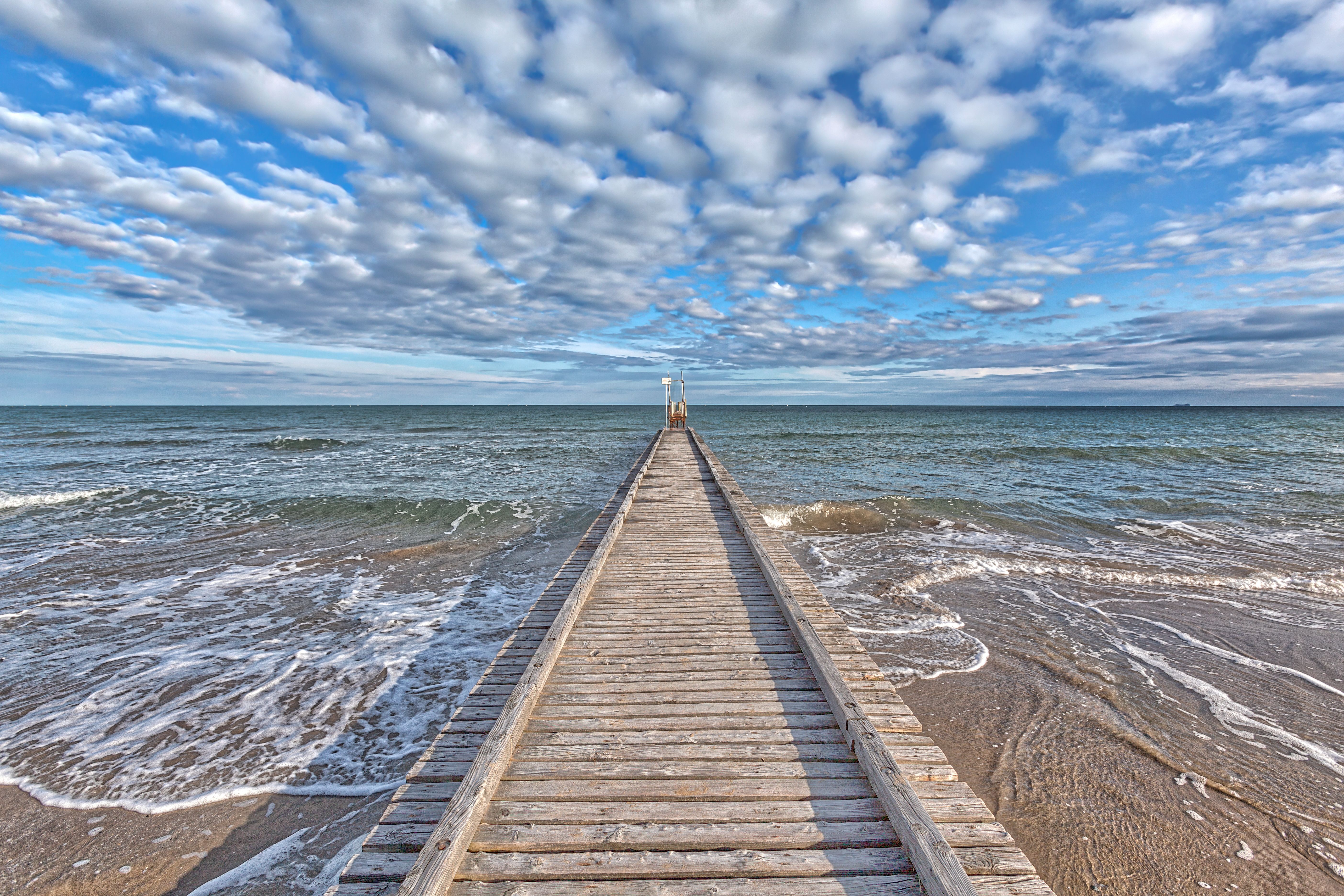 Long pier with sunbleached planks leads out into calm ocean waters.