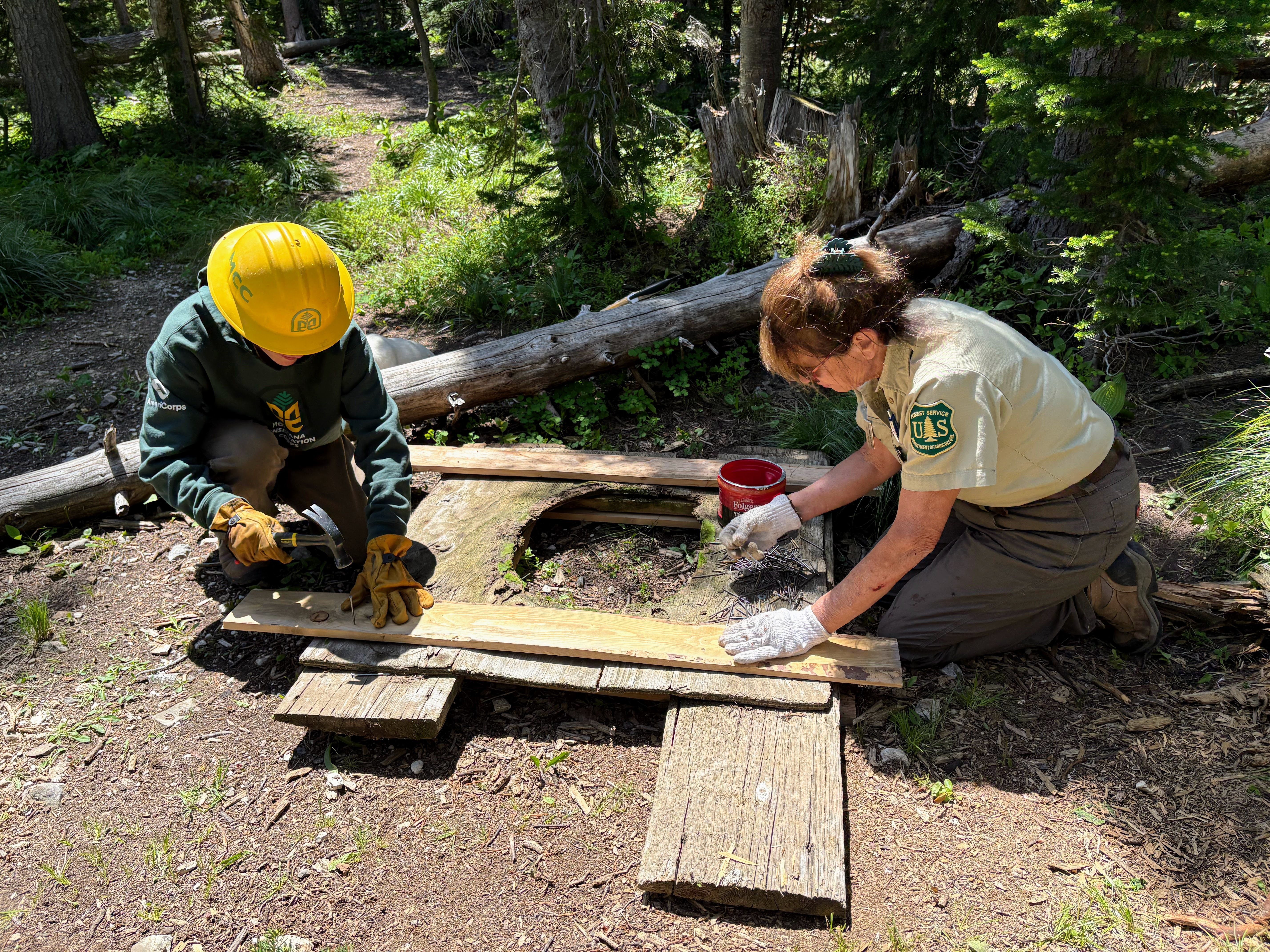 A youth crew member and a USFS employee work on a wood working project together.