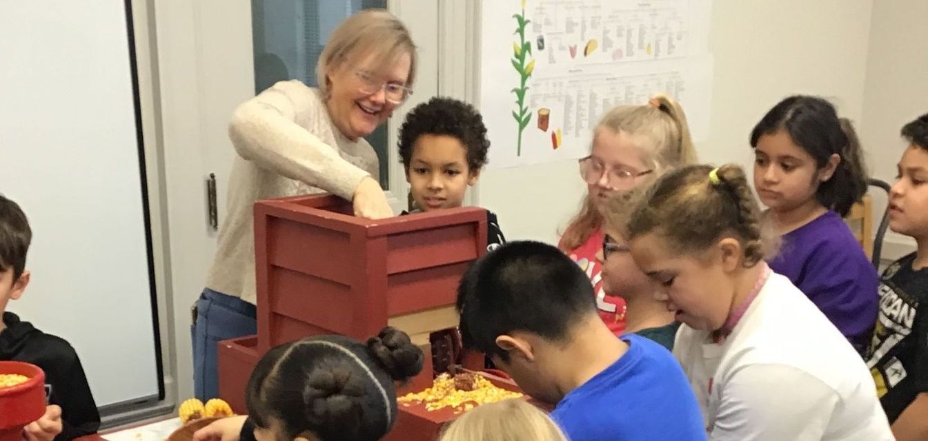 Smoky Hill Museum volunteer teaching a group of children about shelling corn.