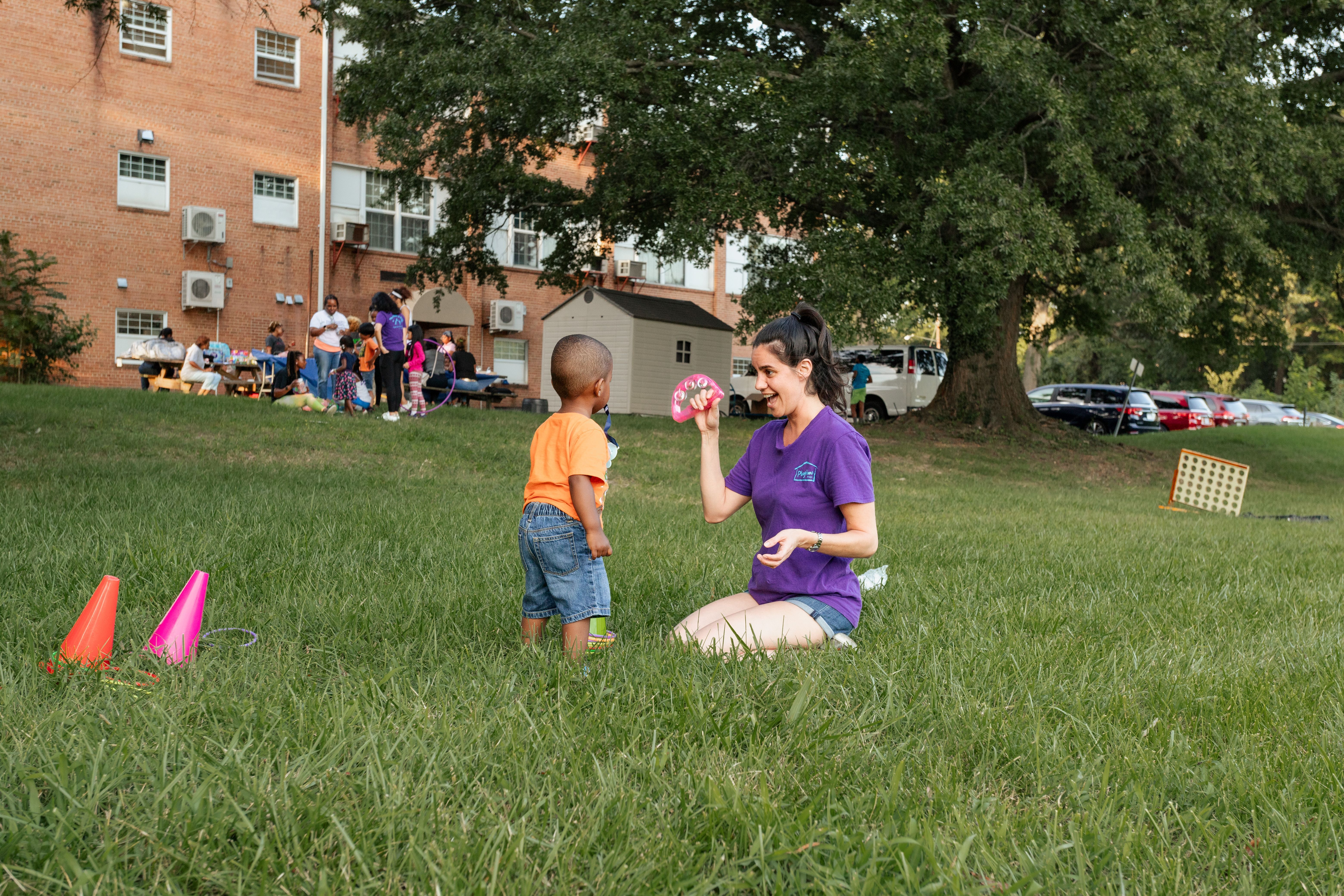 Woman in purple Playtime t-shirt playing with a small boy outside on a grassy field