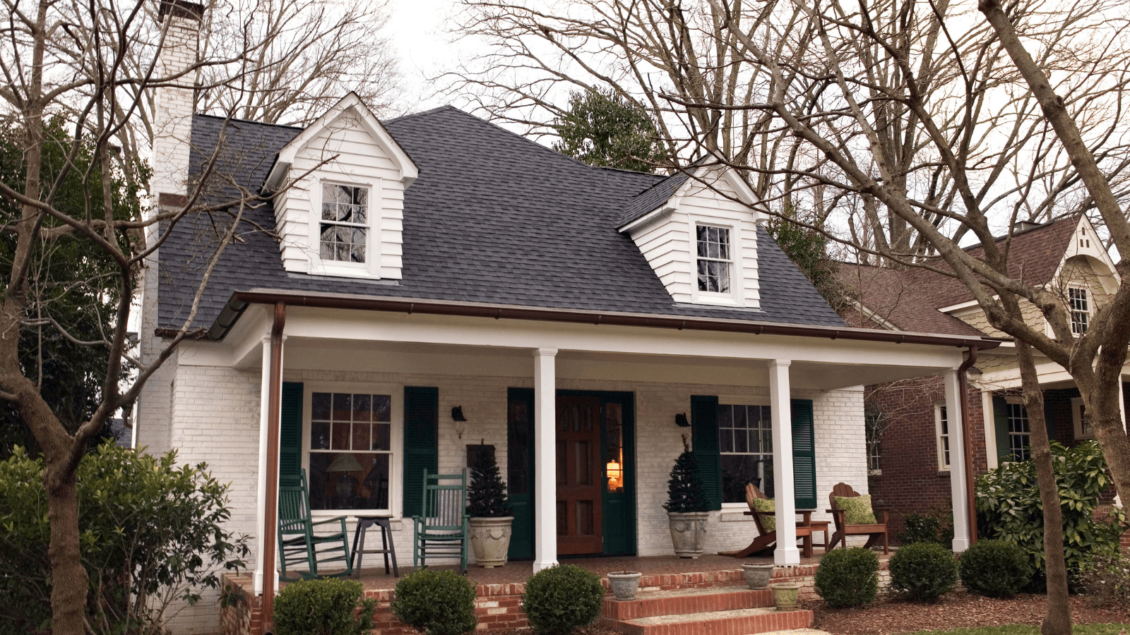 A white house with a red brick porch and bare trees surrounding it 