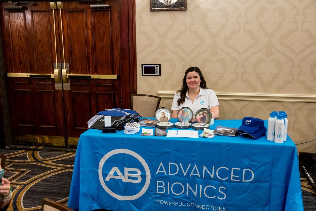 A white woman with brown hair sitting at a table with a blue Advanced Bionics table curtain. 