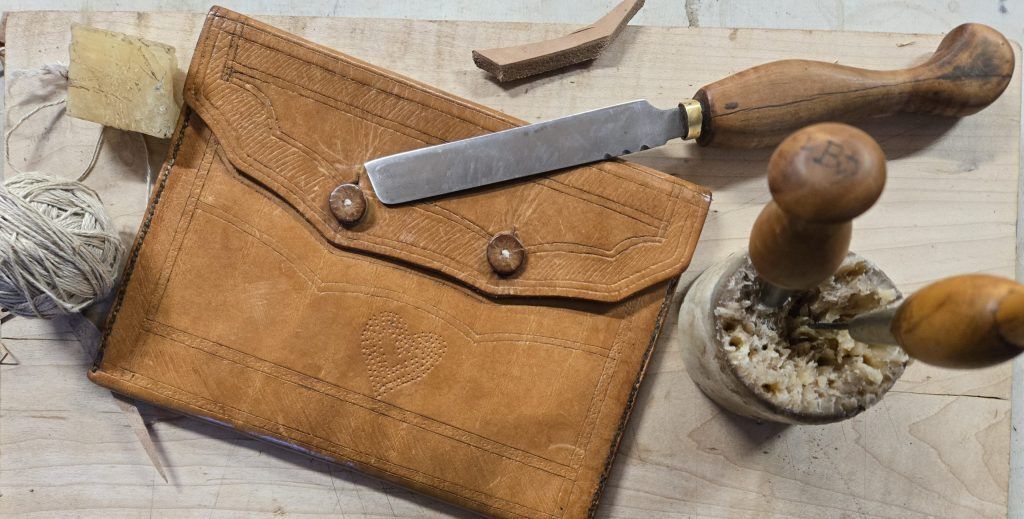 Leather document case surrounded by leatherworking tools.