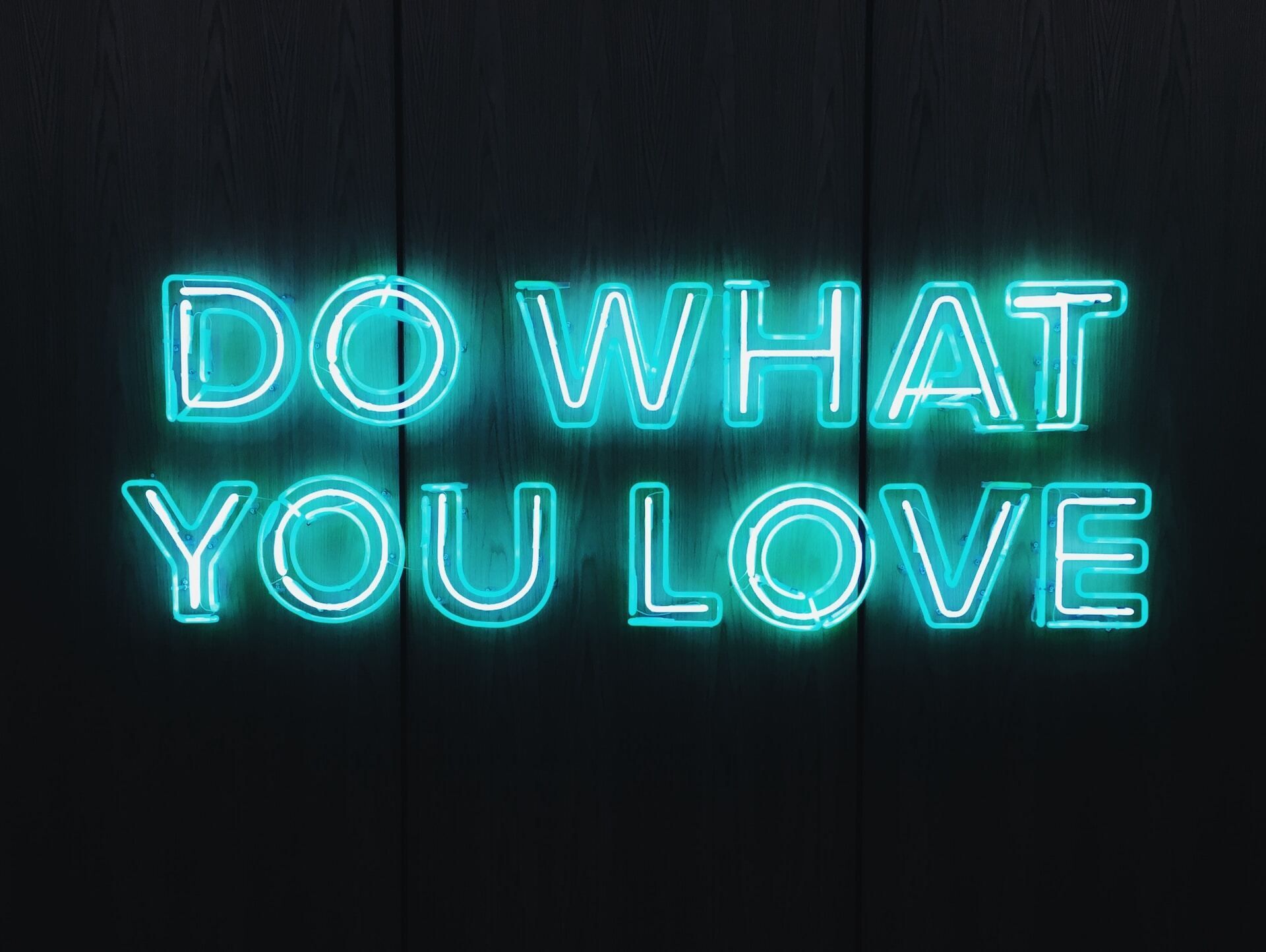 Blue neon sign with dark wood background reading "Do what you love" 