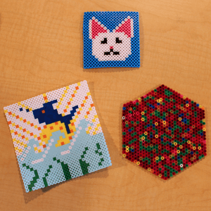 Three beaded shapes laid out. At the top is a white cat in a blue square, below to the left is a fish in the water, and to its right is a multi-colored hexagon.