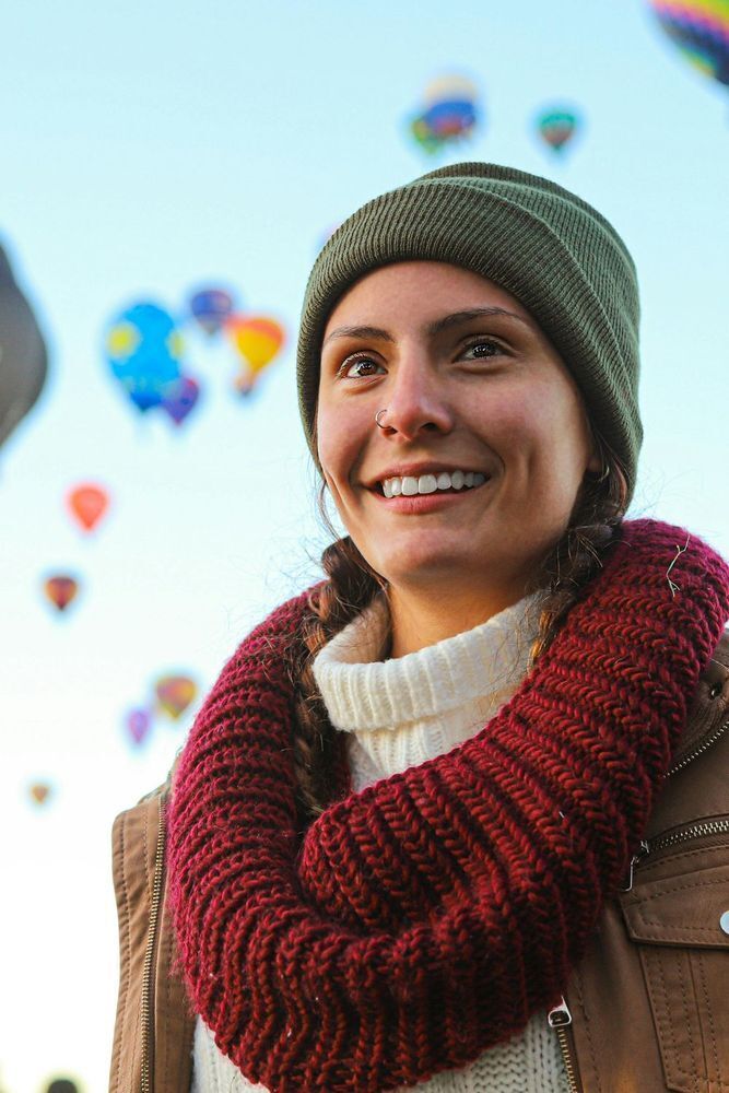 Woman in winter clothes smiling with hot air balloons in the distance flying behind her