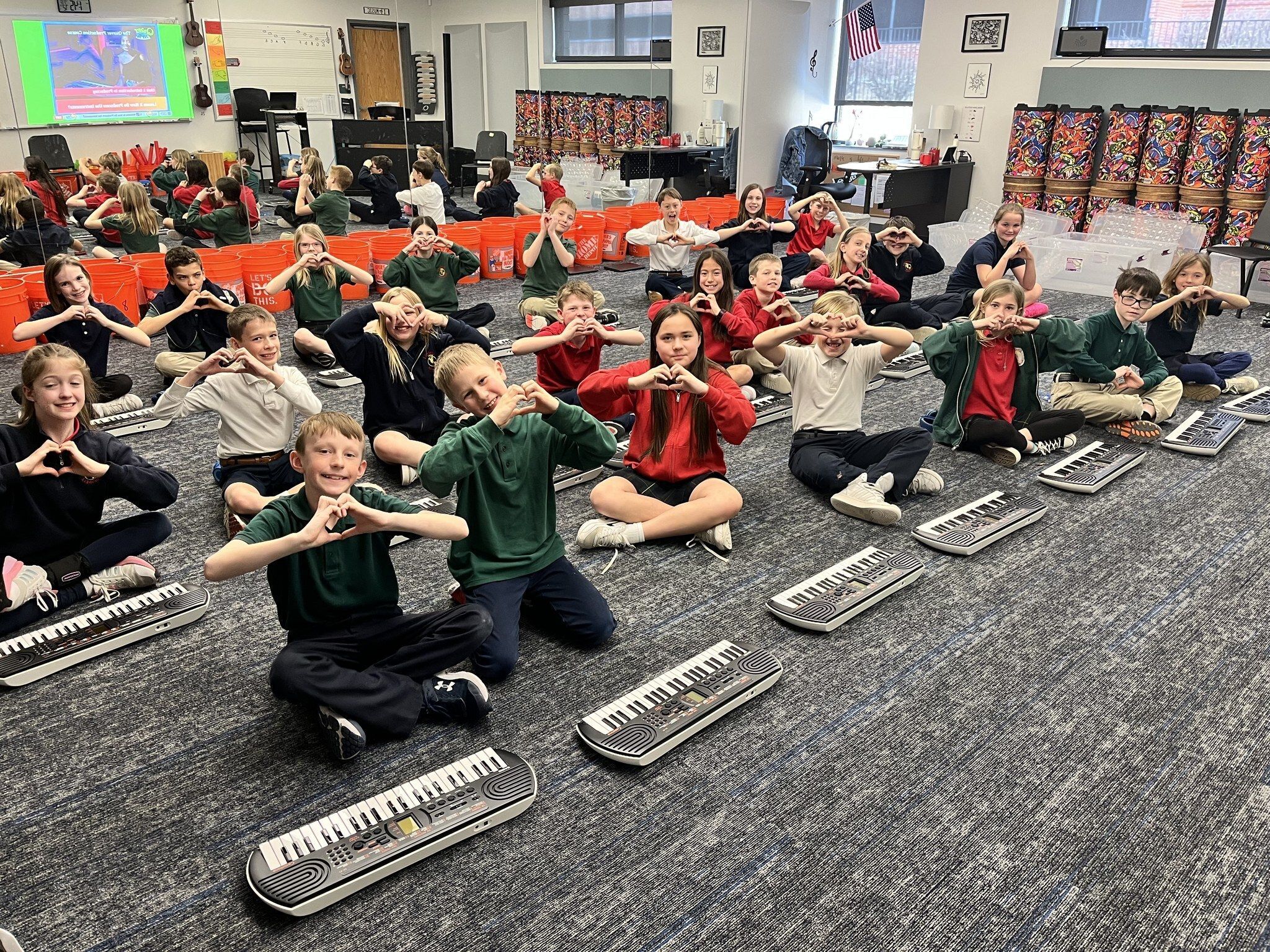 Kids in a music classroom in front on keyboards making heart shapes with their hands