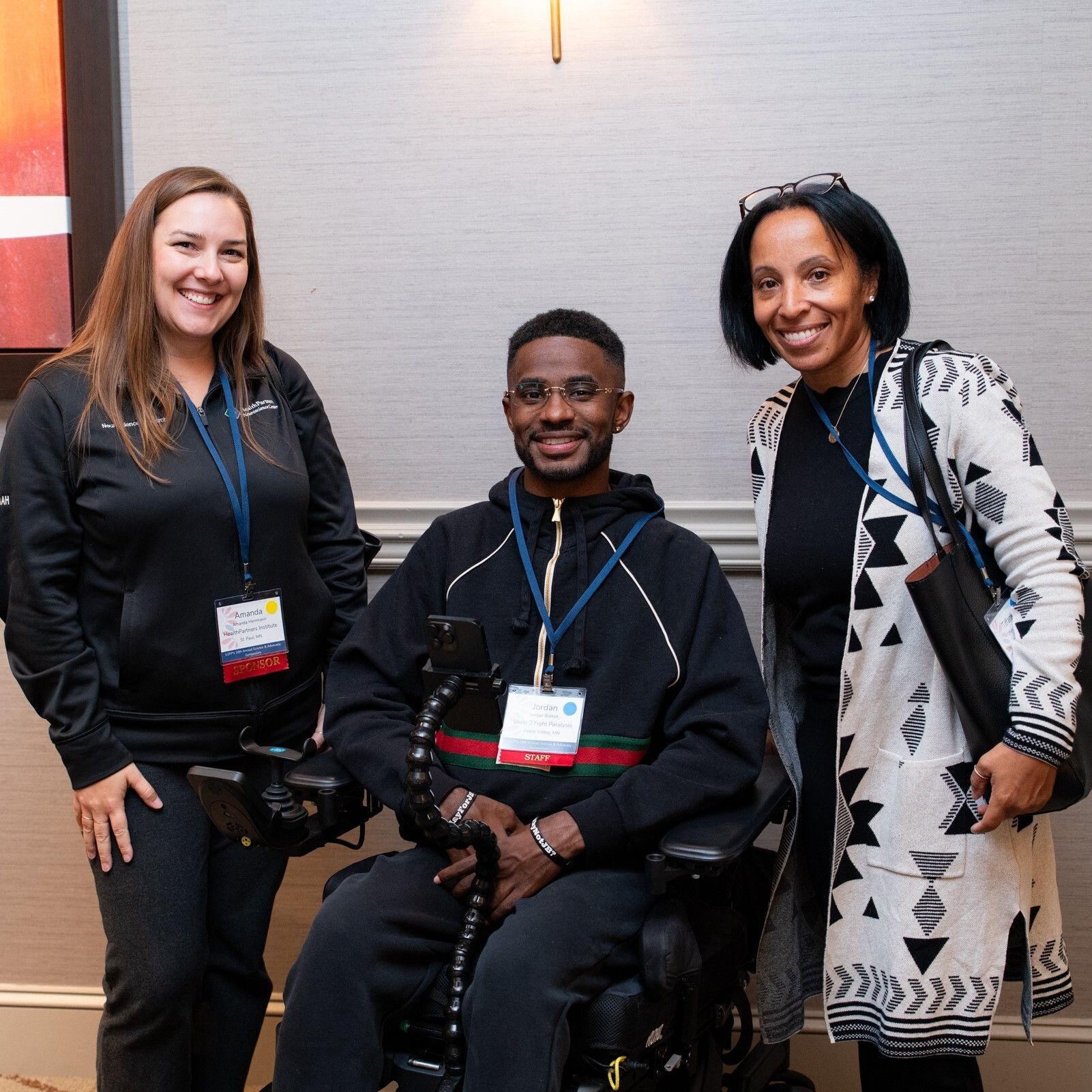 White woman stands to left of a black man in a wheelchair with a black woman standing on the right side of the wheelchair