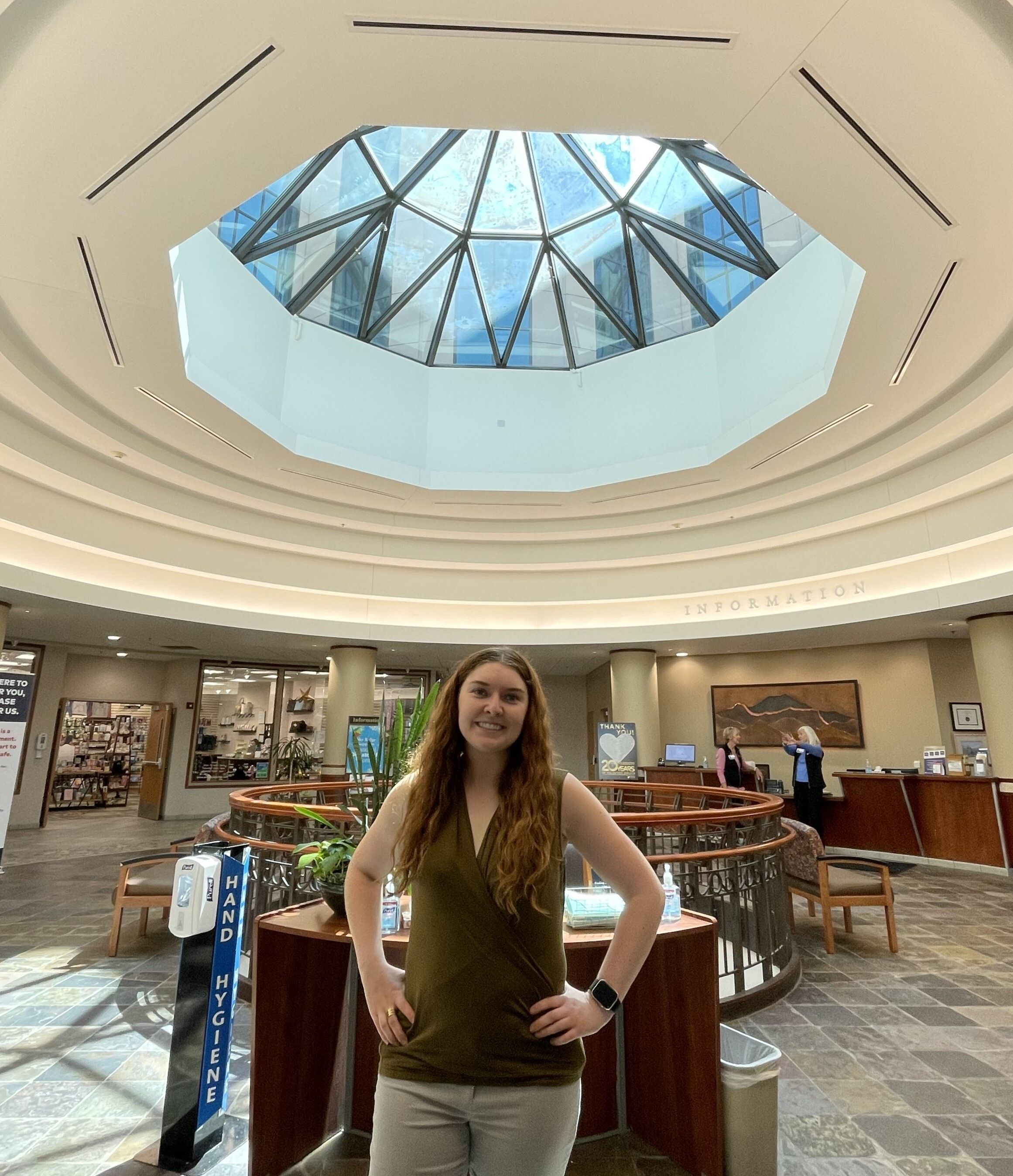 Jazmine standing under a skylight at Sky Ridge Medical Center. Hands on her hips. Smile on her face. 