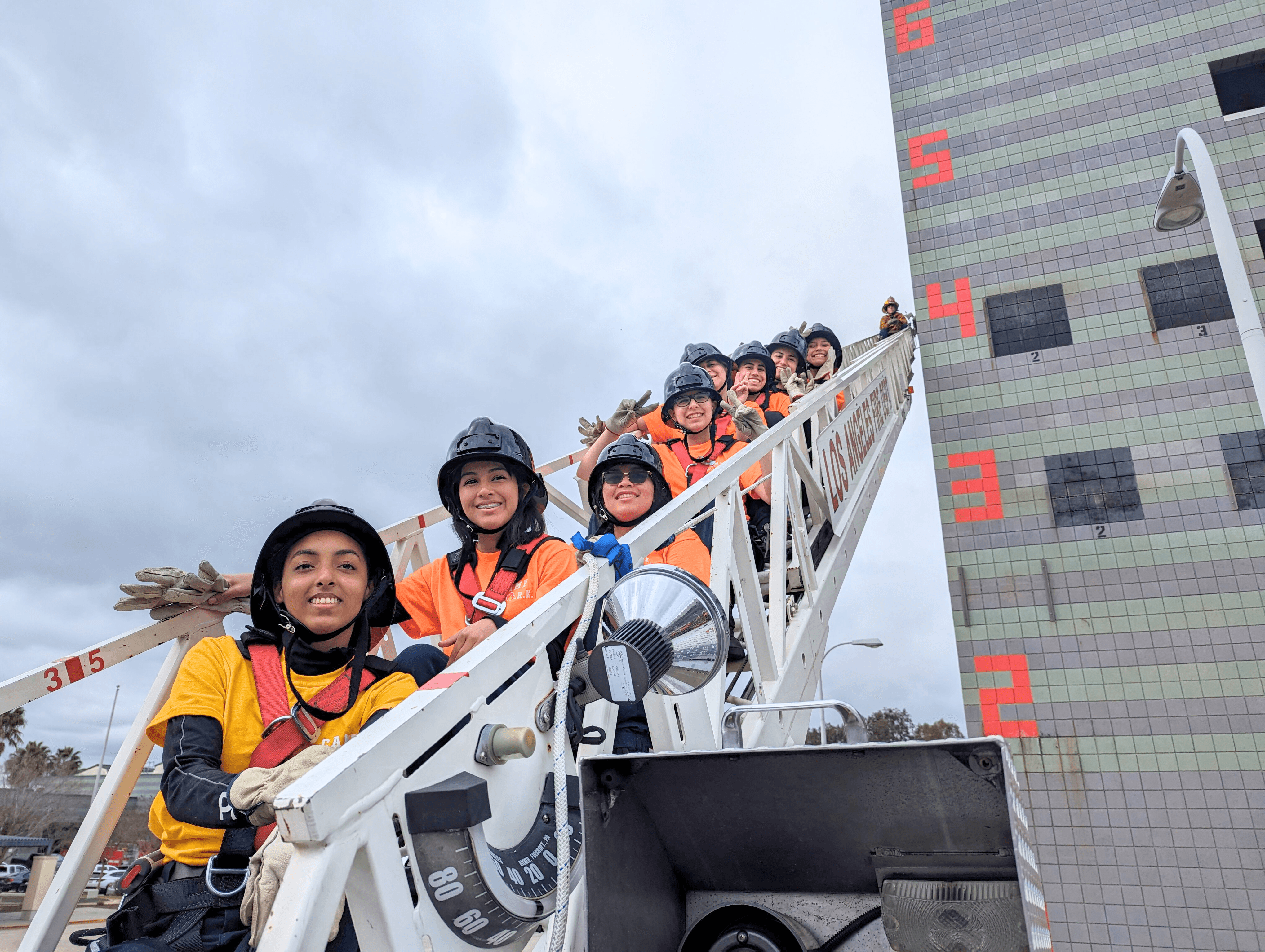 Members of one of the Camp S.P.A.R.K. teams smiling seated on an LAFD aerial ladder.